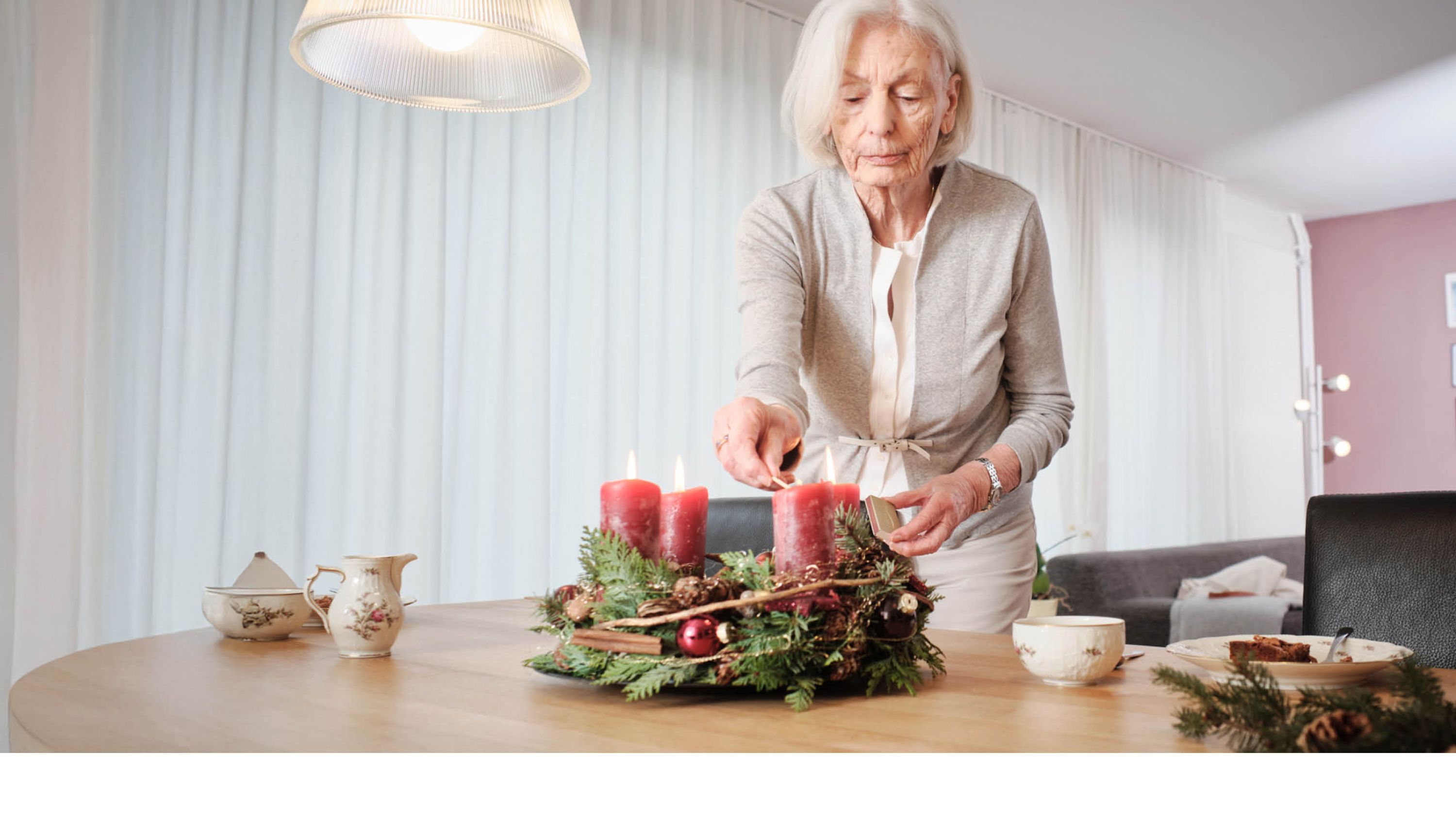 Une femme âgée allume une bougie sur une couronne de l’Avent.