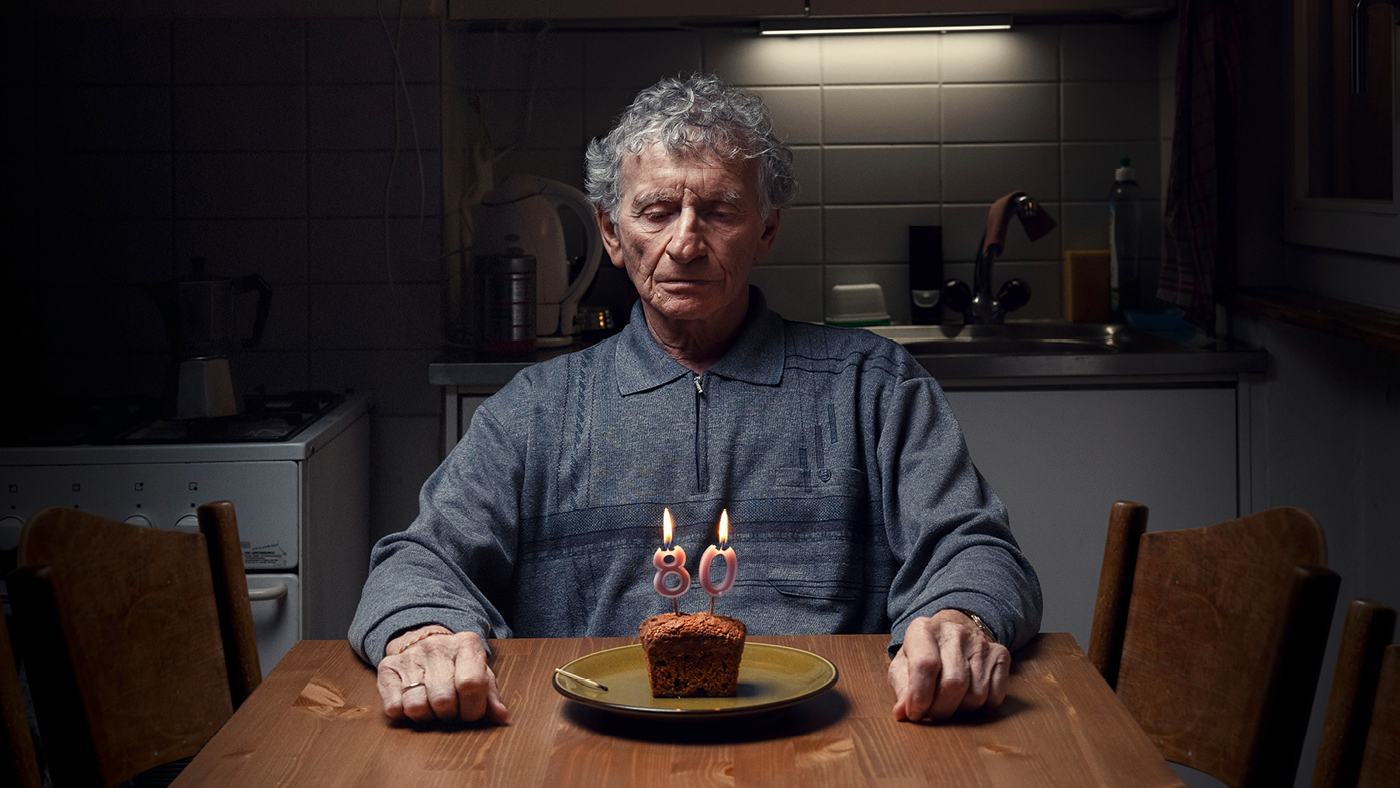 Une personne âgée est assise seule devant un gâteau d'anniversaire.